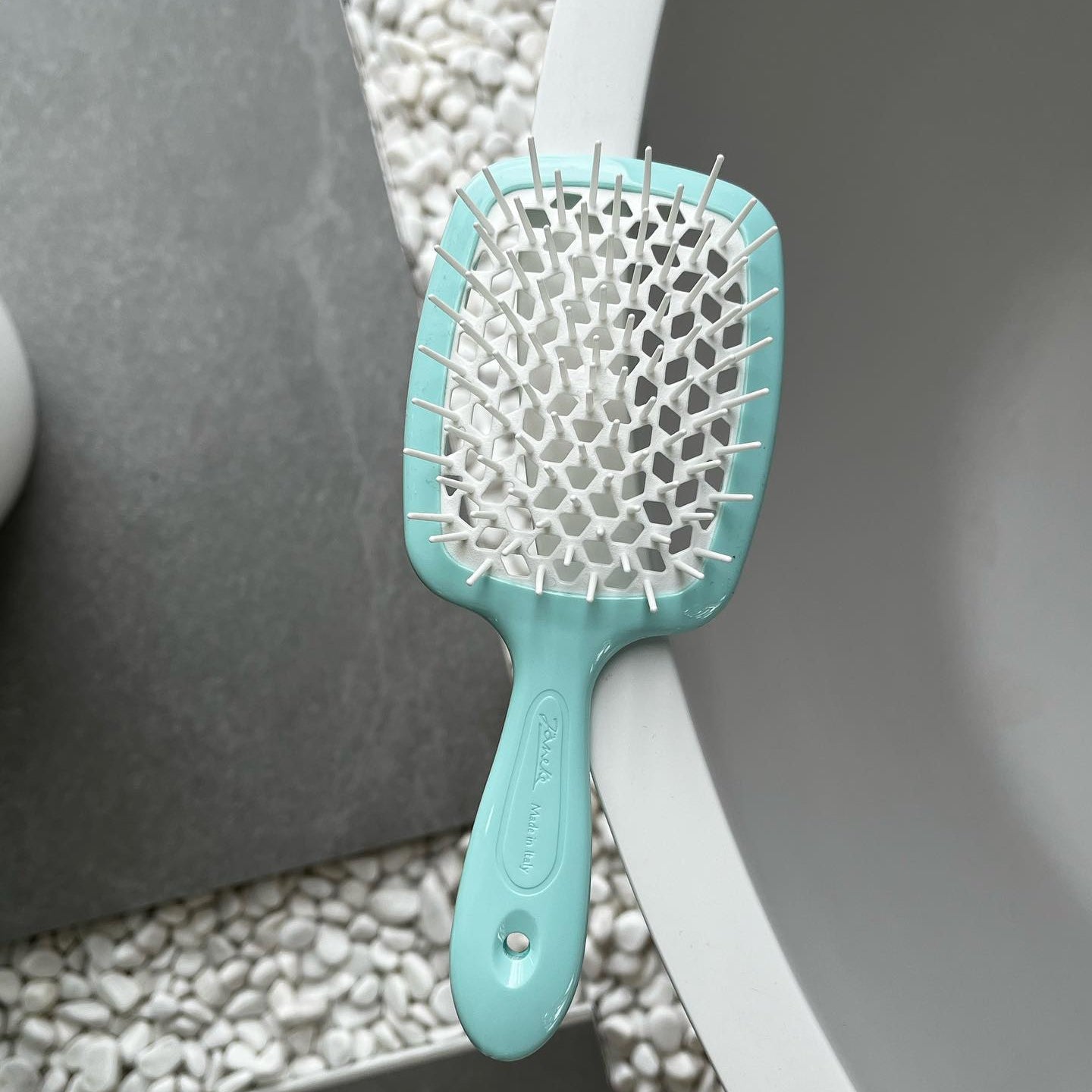 An aqua blue Janeke hairbrush with white bristles on a textured surface