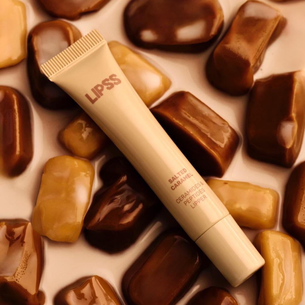 Lip gloss tube lLIPSS Salted Caramel on a background of chocolate candies