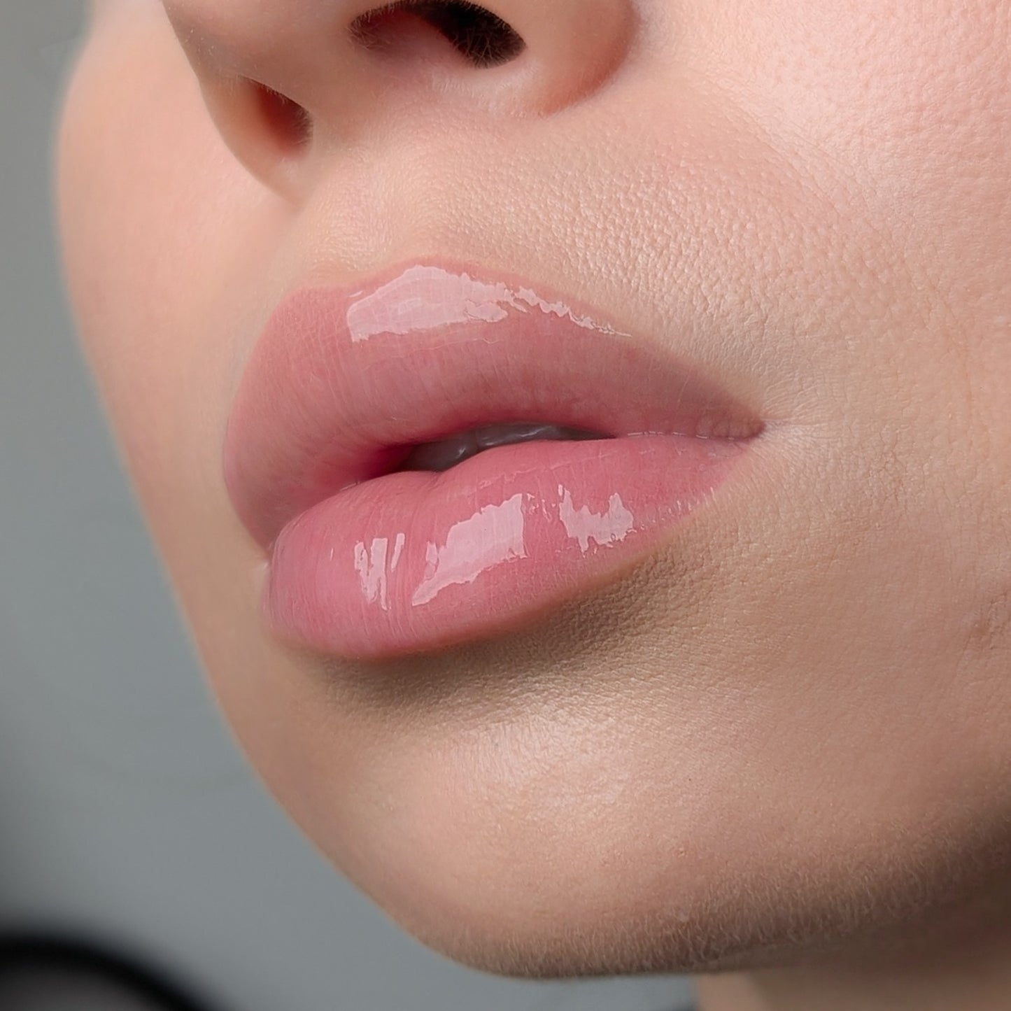 Close-up of a person's lips with a glossy lip gloss Lipss Salted Caramel on a neutral background