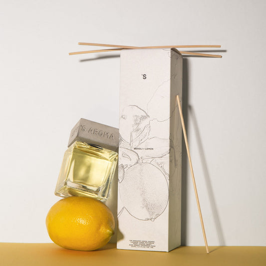 Sister's Aroma reed diffuser Neroli + Lemon with a lemon and its packaging on a yellow surface.
