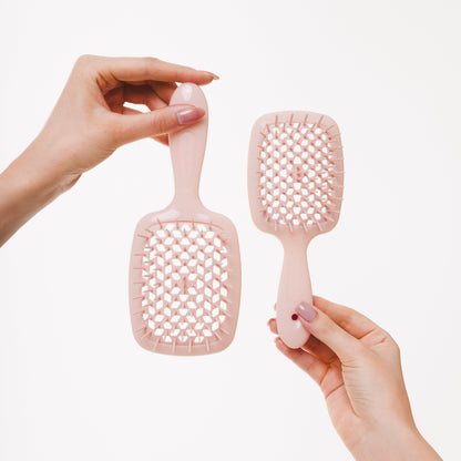 Two powder pink Janeke hairbrushes held by hands against a white background