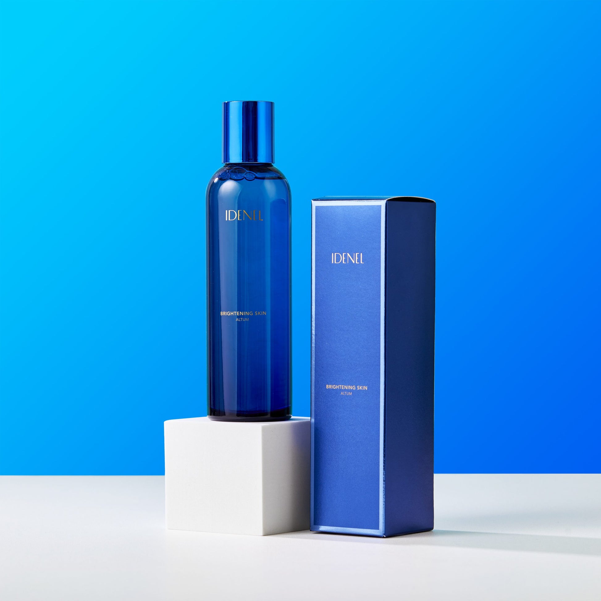 Idenel brightening toner in a blue bottle and packaging on a white platform with a blue background